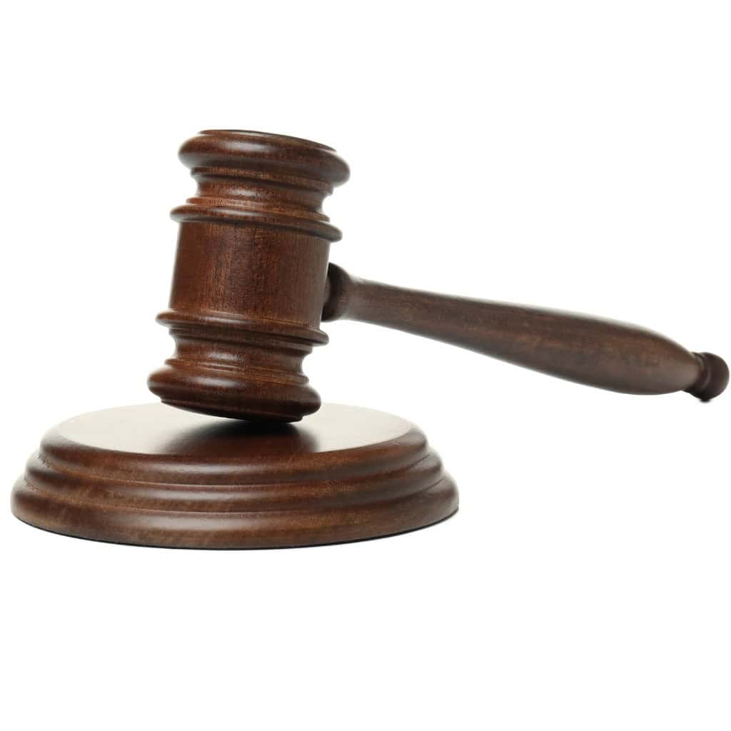 A wooden judge's gavel rests on a round sound block against a white background.